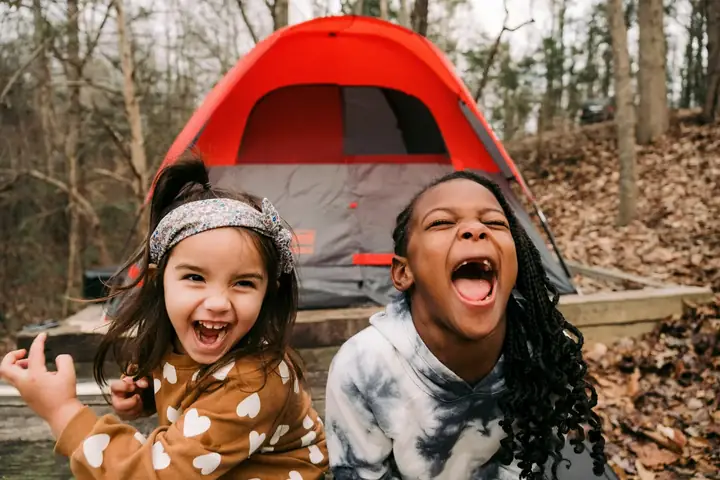 Kids learning camping skills beside a tent in the bush